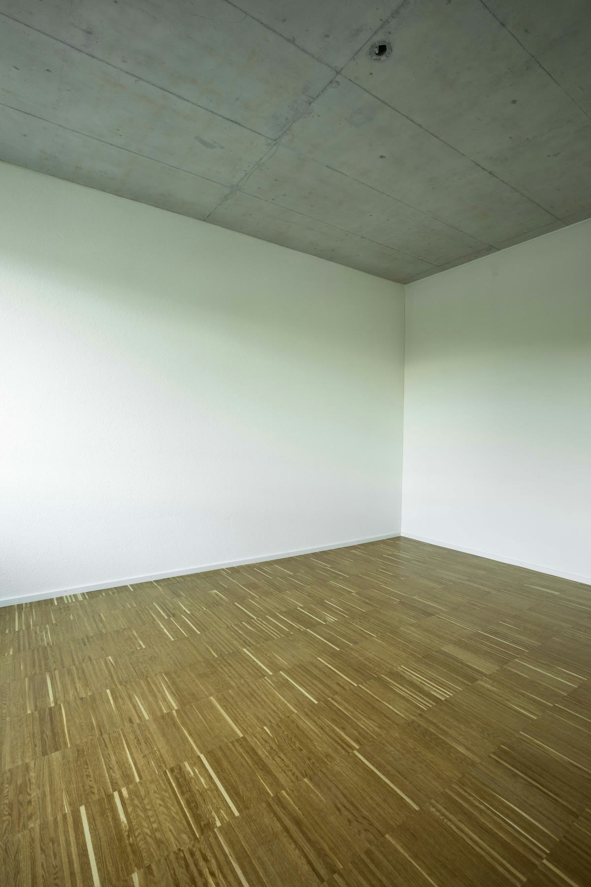 An empty room with pale walls and a bare wood floor, the kind of ordinary interior where what the wall is made of stays invisible until an outlet cover comes off.